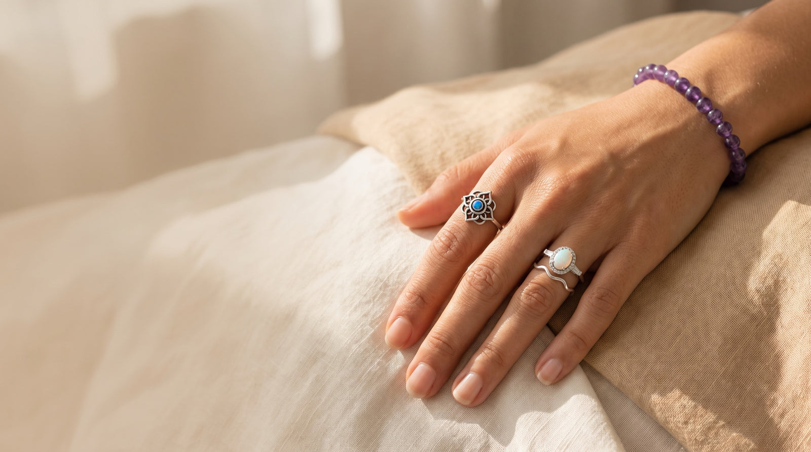A hand wearing a blue opal lotus ring, a white opal halo ring, a wave band and an amethyst bracelet